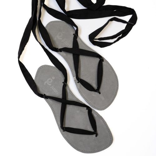 A photo of Juuri ribbon sandals made from leather, viscose, and rubber soles. The sandals have a grey footbed and long black laces. Both sandals are shown from above facing diagonally right against a white background. #color_grey-black