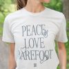 Tan "Peace, Love, Barefoot" T-shirt shown on a tan woman with brown hair with grass and woods in the background.