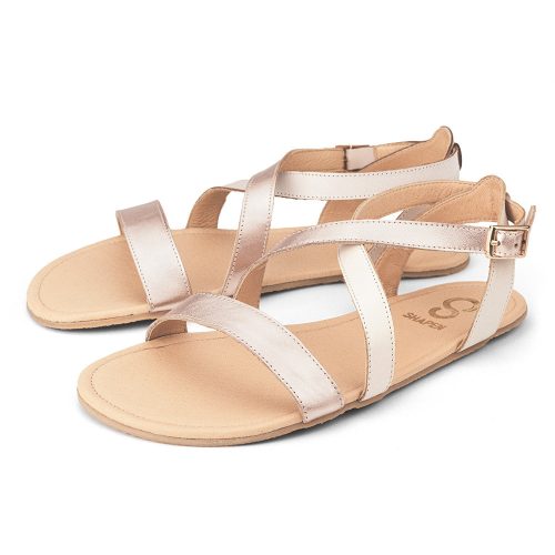 A photo of Rose Gold Shapen Calla Sandals made with leather and tan rubber soles. The sandals have a slight sparkle on the toe strap and one of the foot crossing straps. The other foot crossing strap is a creamy white. Both sandals are shown from the left side beside each other against a white background in this photo. #color_rose-gold