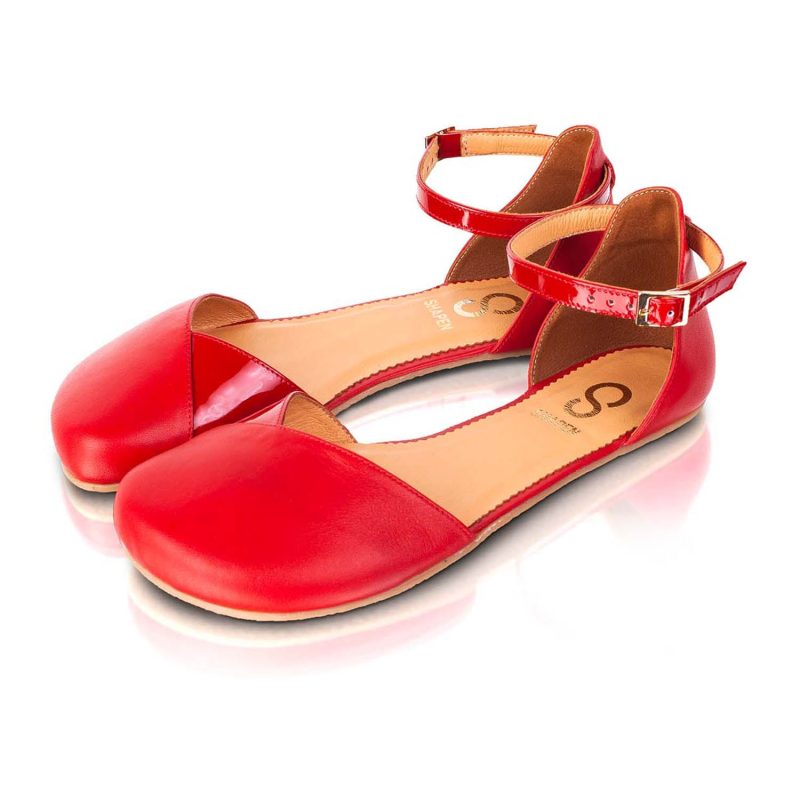 A photo of Shapen Poppy D’orsay dressy flats with a leather upper and rubber soles. The flats are a cherry red color with a heel cup and dainty ankle strap, the inside of the sole are a beige color. Both flats are shown beside each other turned with the right shoe towards the front against a white background. #color_cherry