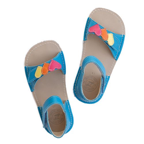 A photo of the Zeazoo Ariel kids leather sandals. The sandals are blue in color and have velcro straps that go over the toes and around the ankles. The toe straps have a yellow, orange, and pink heart on them. The sandals are shown together from above on a white background. #color_light-blue-hearts